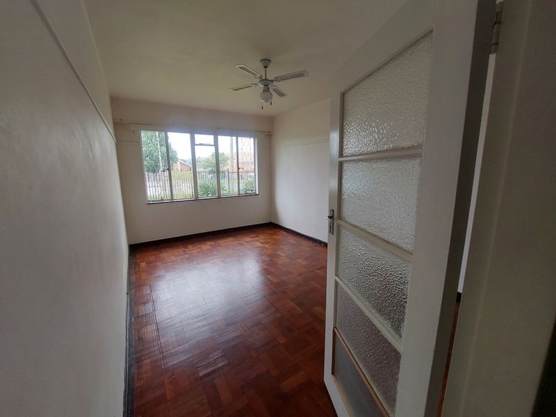 An empty bedroom featuring original parquet flooring, a ceiling fan, and a classic textured glass panel door.