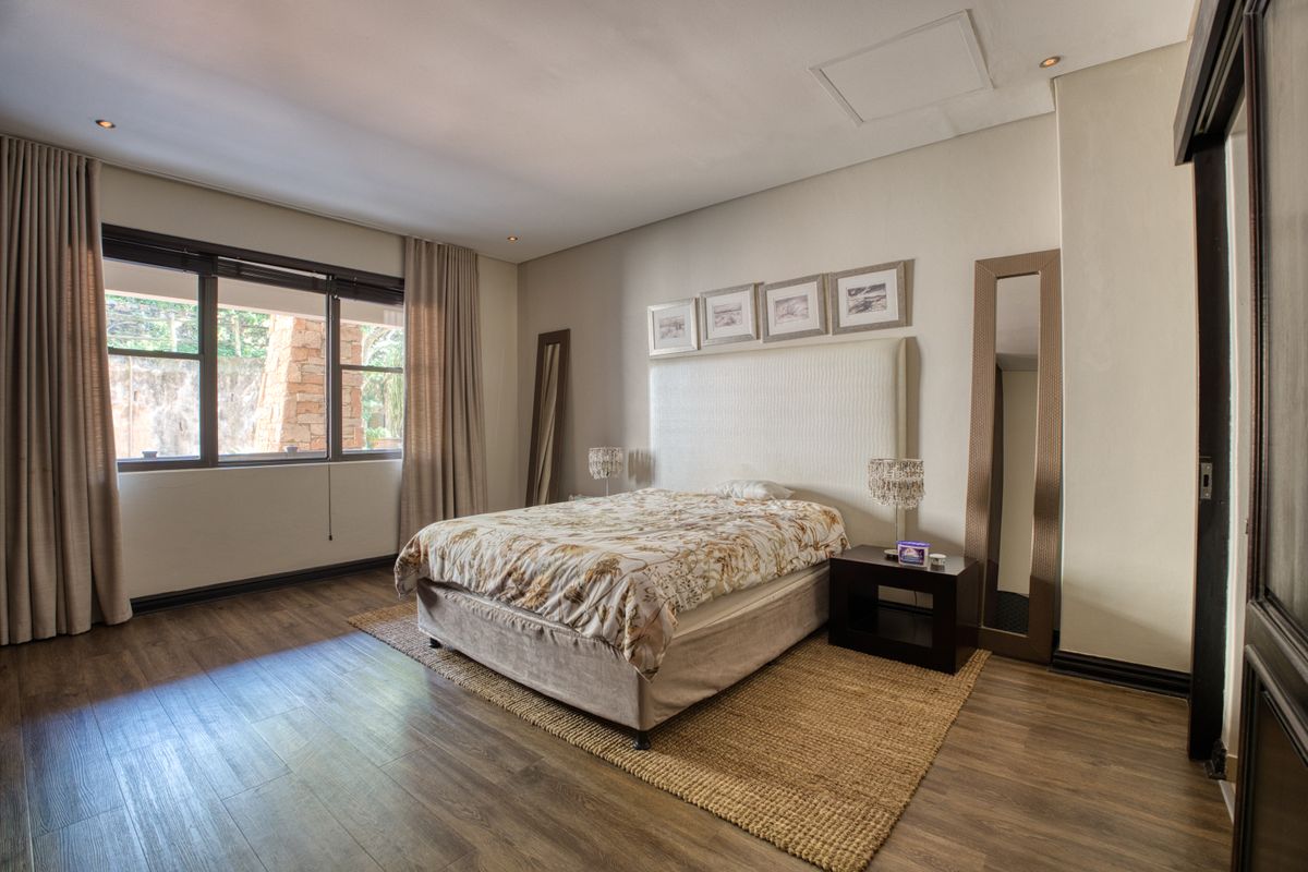 A spacious bedroom featuring wood-look flooring, recessed ceiling lighting, and large windows with neutral curtains, offering a comfortable and well-maintained living space.