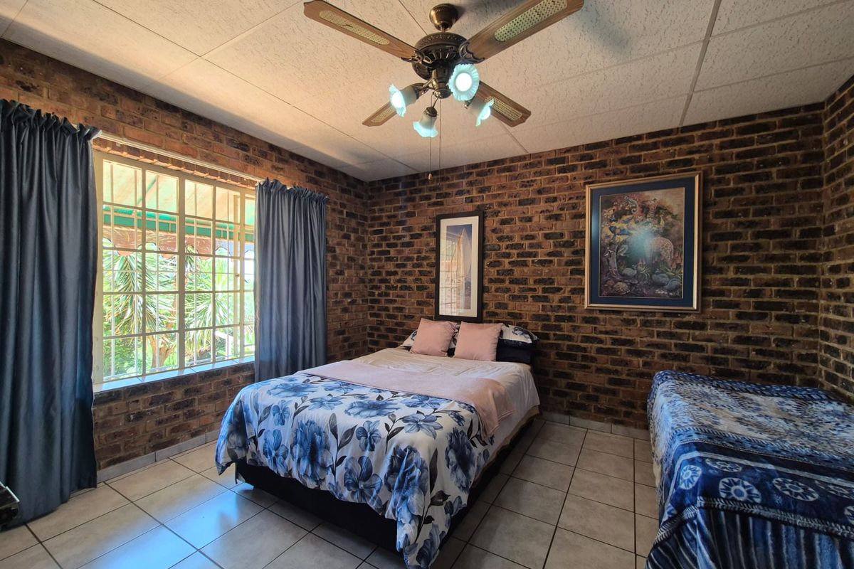 A bedroom featuring exposed brick walls, tiled flooring, and a ceiling fan, offering a rustic aesthetic with natural light from the window.