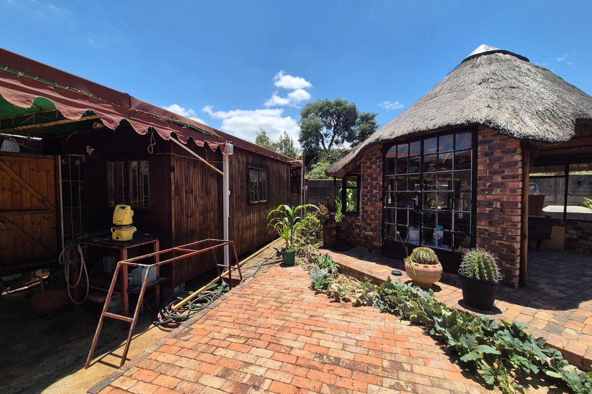 Outdoor area featuring a brick-built structure with a traditional thatch roof and adjacent timber-clad building, set on a paved courtyard.