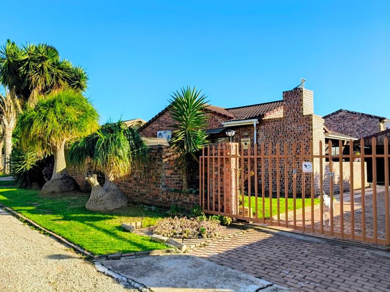 Front view of a face brick house featuring a tiled roof, chimney, and secure metal gate entrance with a paved driveway.