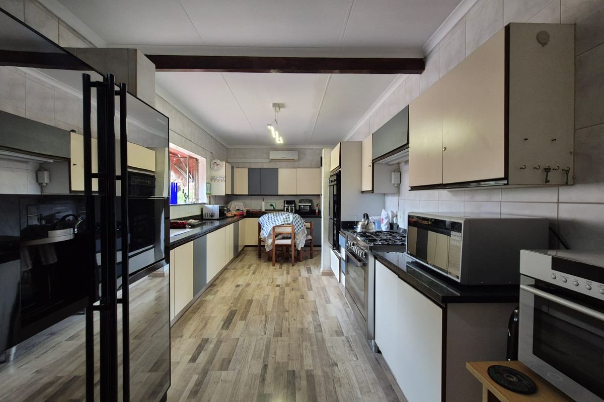 A spacious galley-style kitchen featuring extensive cabinetry, dark countertops, a built-in oven, and a gas hob, with a dedicated dining area at the far end.