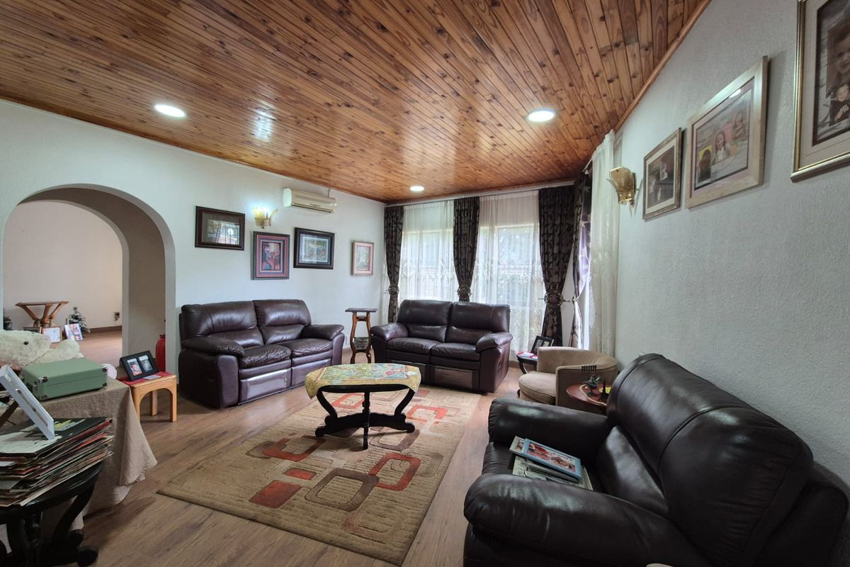 A spacious living room featuring a distinctive timber-paneled vaulted ceiling, laminate flooring, and an arched entryway leading to adjacent living areas.