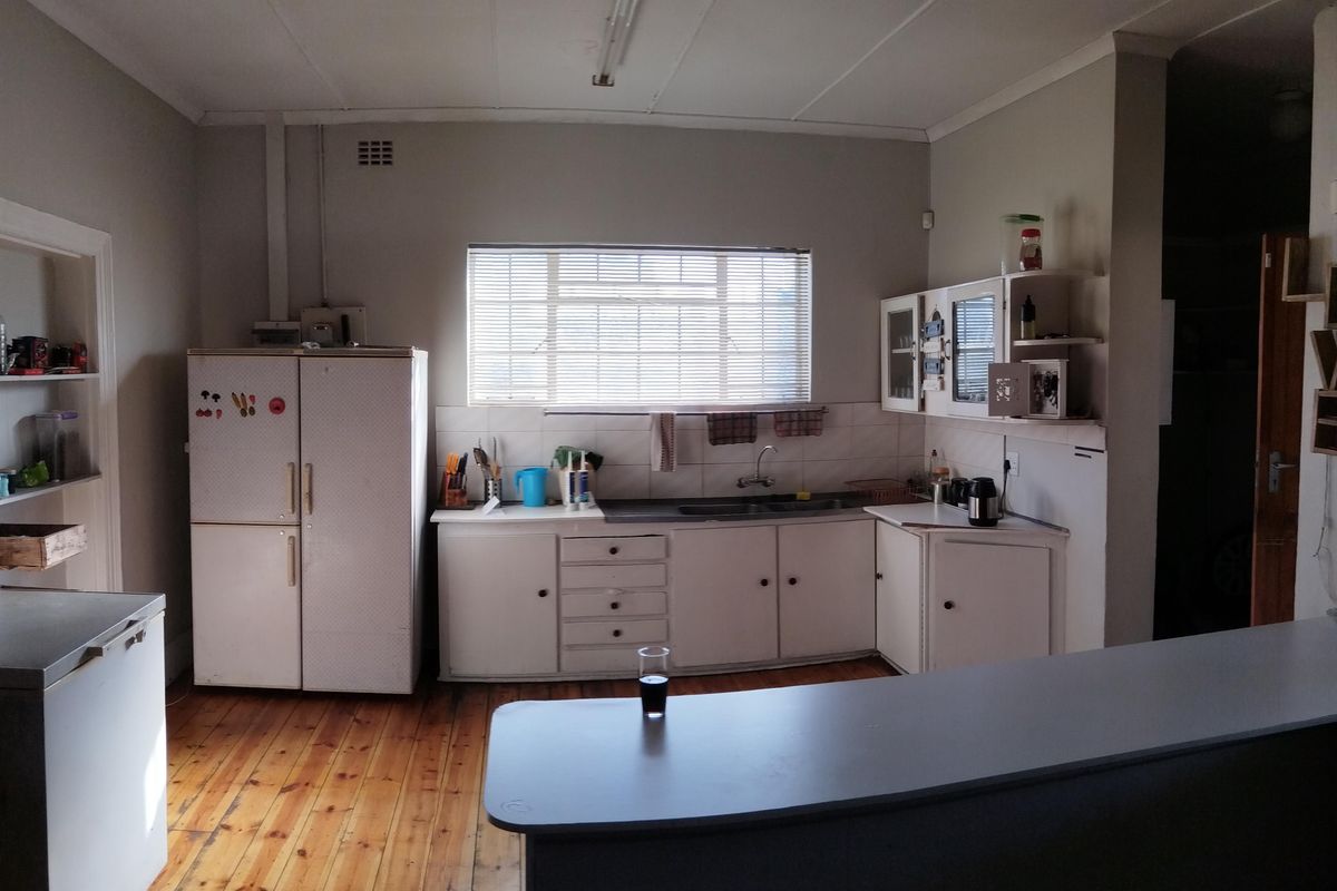 A functional kitchen featuring timber flooring, white cabinetry, a double sink, and a breakfast bar counter, offering a classic layout with potential for modernization.
