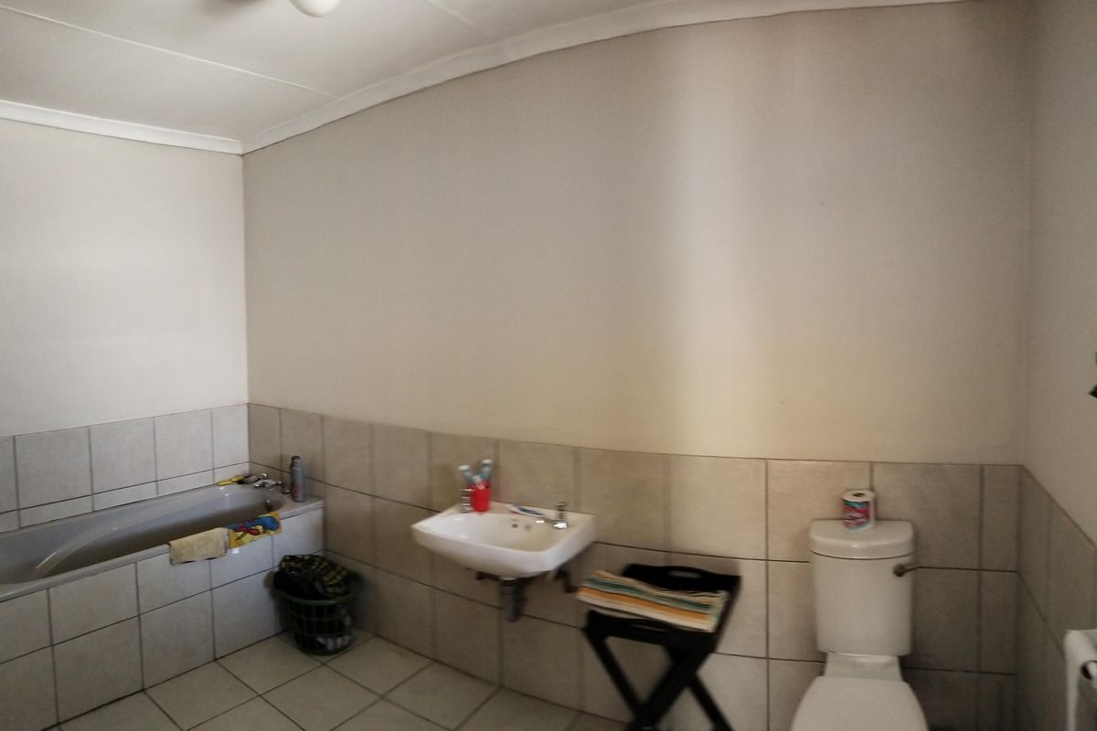 A functional bathroom featuring a built-in bathtub, wall-mounted basin, and standard toilet with neutral tiled flooring and partial wall tiling.
