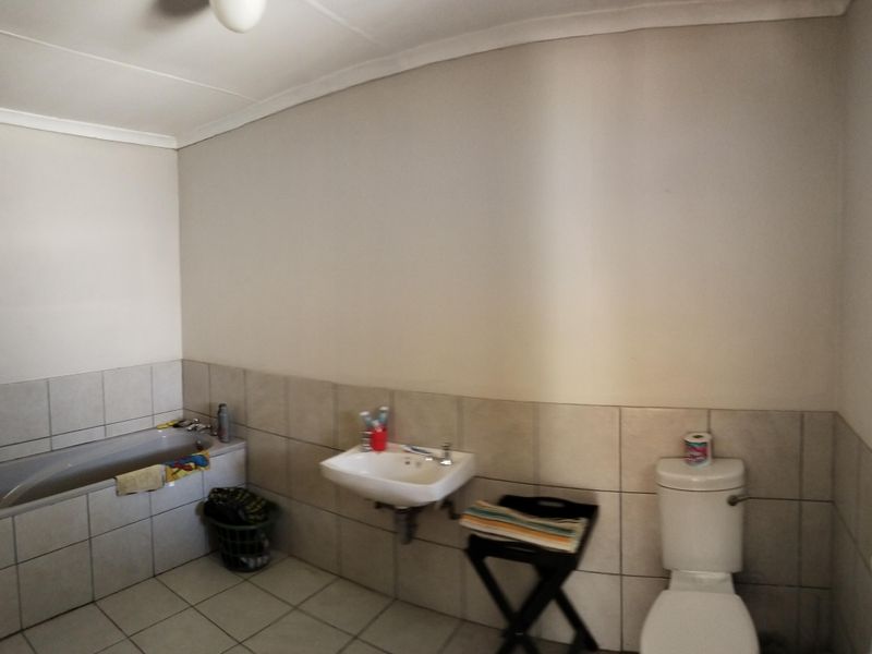 A functional bathroom featuring a built-in bathtub, wall-mounted basin, and standard toilet with neutral tiled flooring and partial wall tiling.