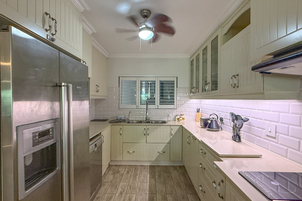 A well-appointed kitchen featuring shaker-style cabinetry, subway tile backsplash, stone countertops, integrated appliances, and a ceiling fan.