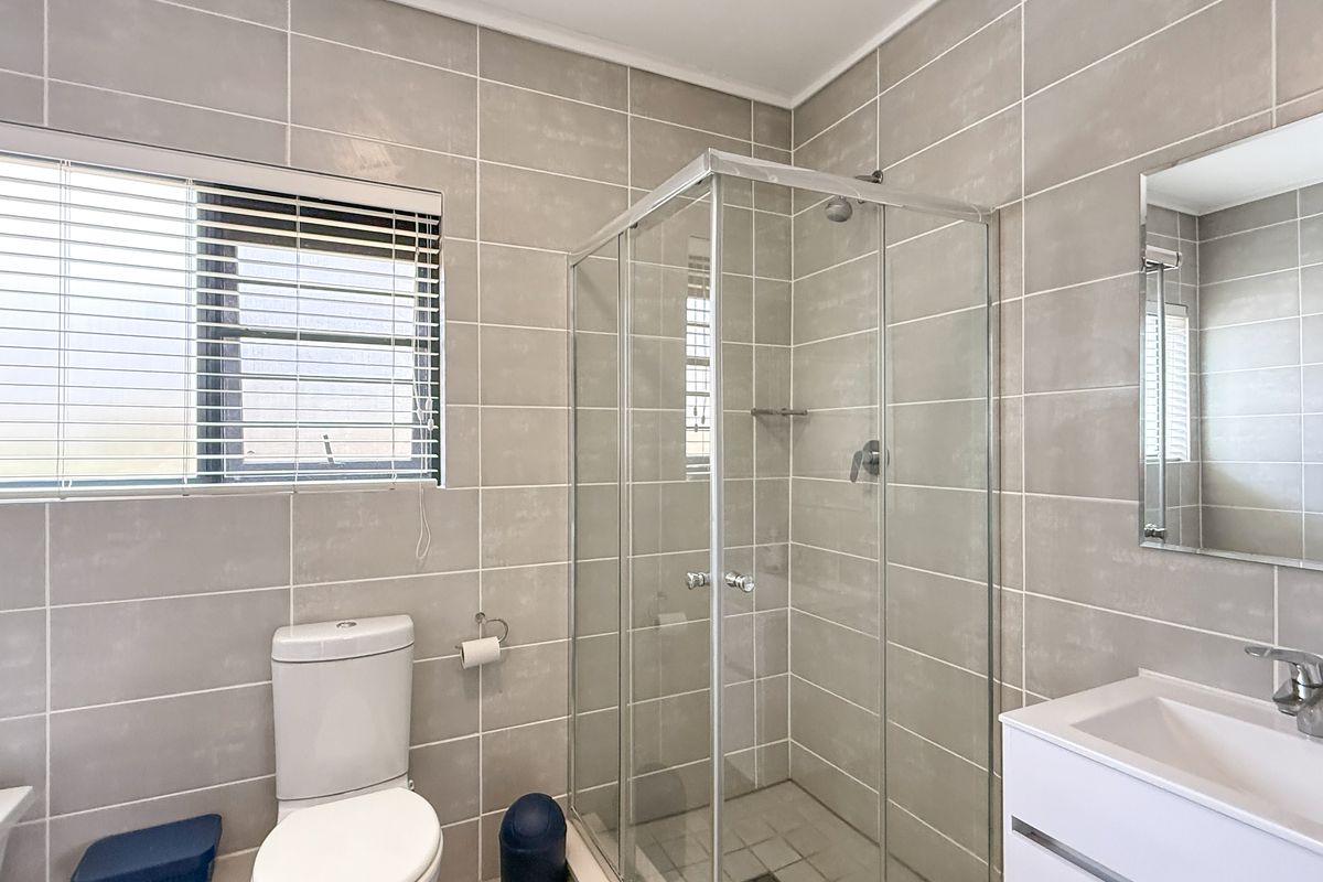 Modern bathroom featuring a glass-enclosed shower, wall-mounted vanity with basin, and neutral floor-to-ceiling tiling.