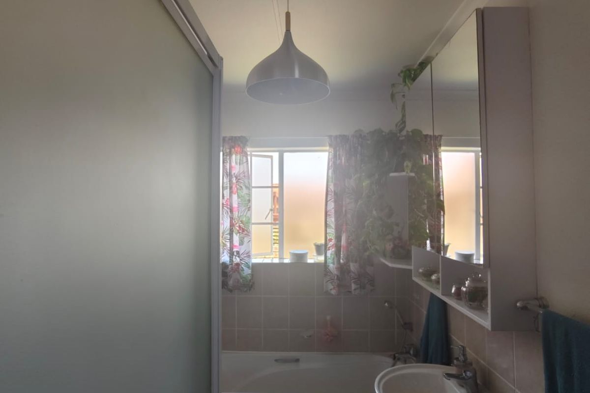 A functional bathroom featuring a built-in bathtub, pedestal basin, and mirrored medicine cabinet with tiled splashbacks.