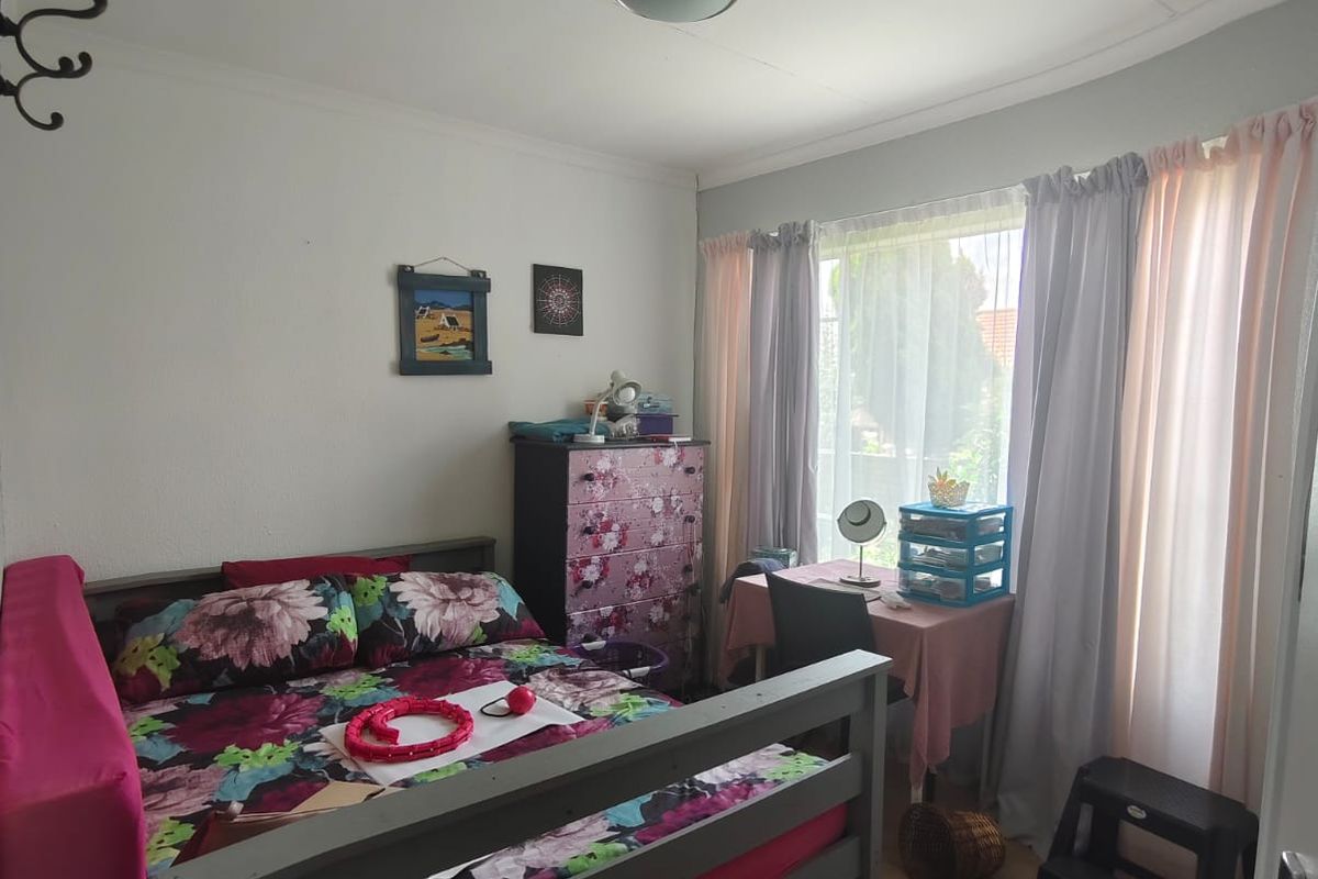 A functional bedroom featuring laminate flooring, a large window with curtain tracks, and a central ceiling light fixture.