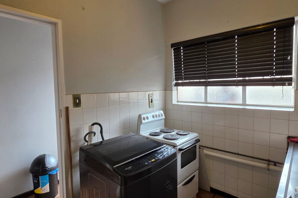 A functional kitchen area featuring tiled splashbacks, a freestanding electric stove, and dedicated space for laundry appliances under a window with blinds.