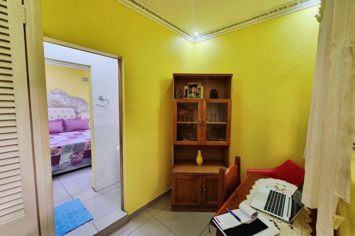 A view from a yellow-walled room looking into an adjacent bedroom, featuring tiled flooring and decorative crown molding.