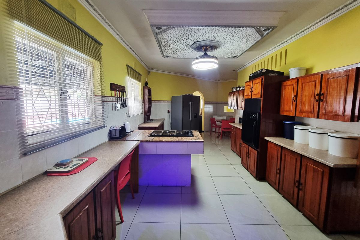 Spacious kitchen featuring wooden cabinetry, a central island with a built-in hob, tiled flooring, and ample counter space.