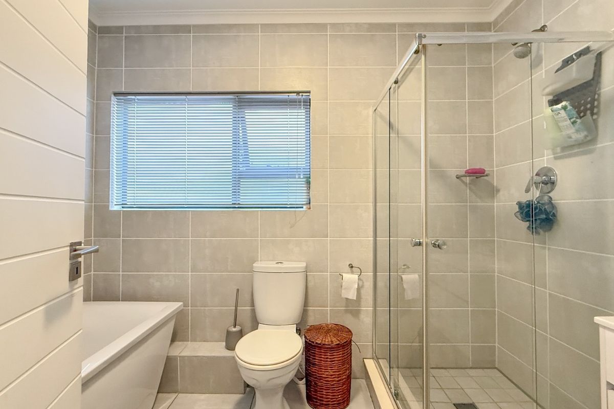 Modern bathroom featuring a glass-enclosed shower, a separate bathtub, neutral wall tiling, and a window with fitted blinds.