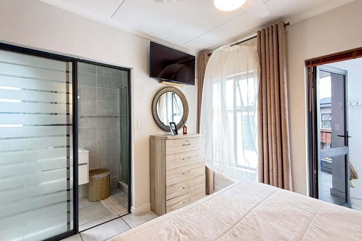 A well-maintained bedroom featuring an en-suite bathroom with a glass sliding door, tiled flooring, and direct access to a private balcony.