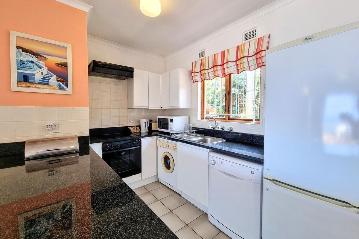 A functional kitchen featuring dark granite countertops, white cabinetry, a built-in oven with extractor fan, and integrated laundry and dishwasher appliances.
