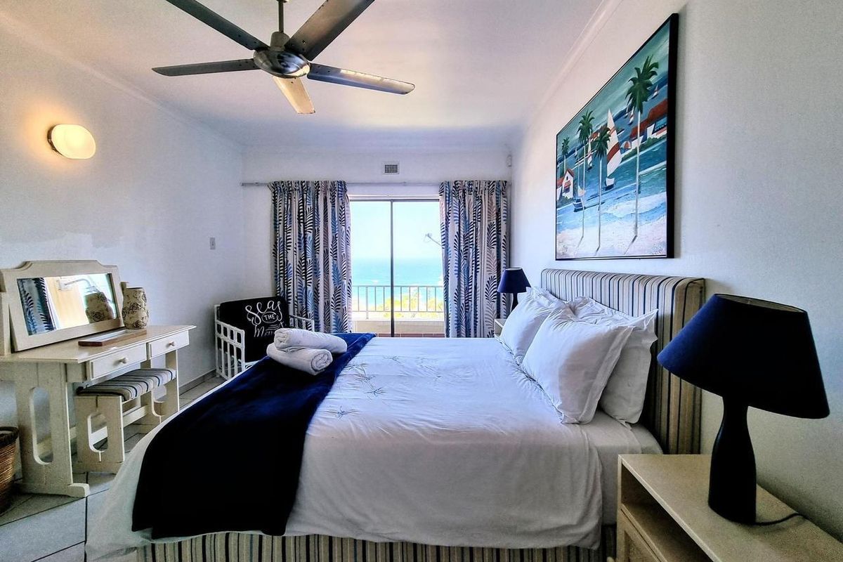 A bright bedroom featuring a ceiling fan and sliding glass doors that open onto a balcony with ocean views.