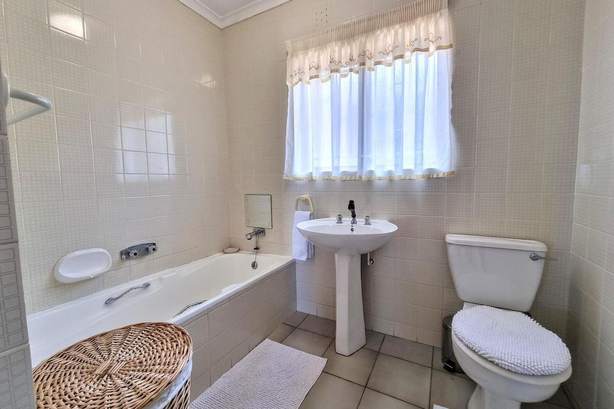 A functional bathroom featuring a bathtub, pedestal basin, and toilet, finished with neutral wall and floor tiles.