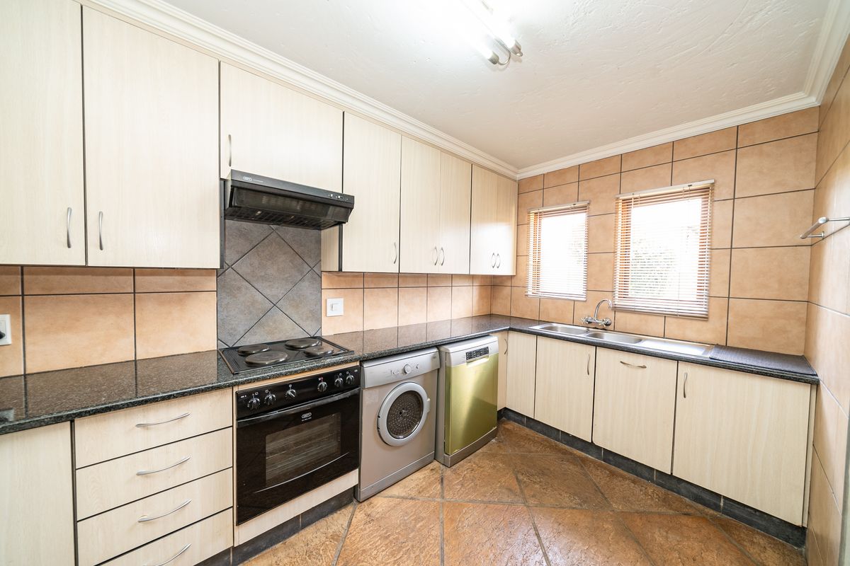 A functional kitchen featuring light-toned cabinetry, granite countertops, a built-in oven with extractor fan, and integrated space for laundry appliances.