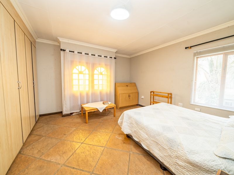 A bedroom featuring built-in wooden cupboards, tiled flooring, and natural light through arched and standard windows.