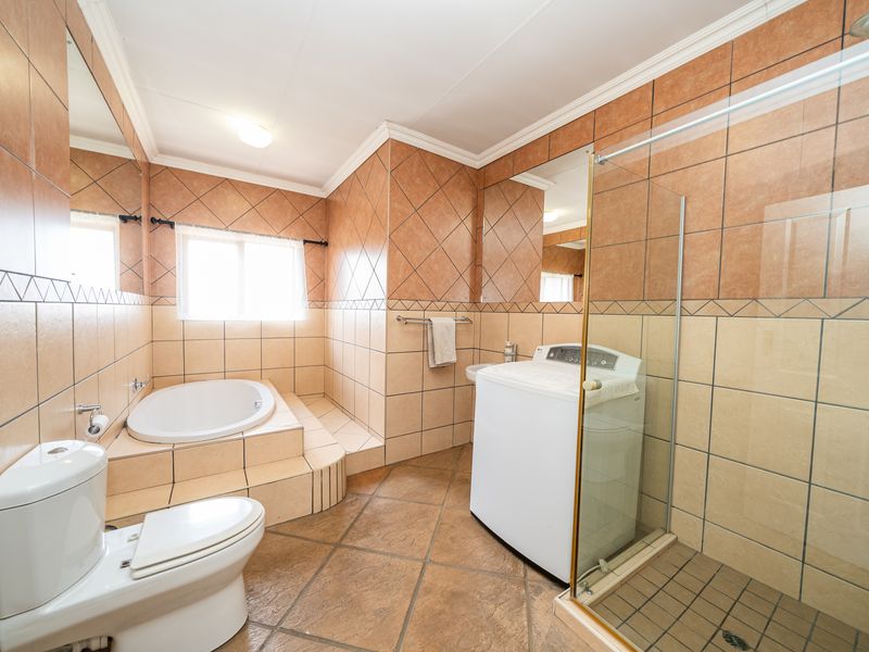 Spacious bathroom featuring a built-in corner bathtub, glass-enclosed shower, toilet, and integrated laundry area with tiled finishes throughout.