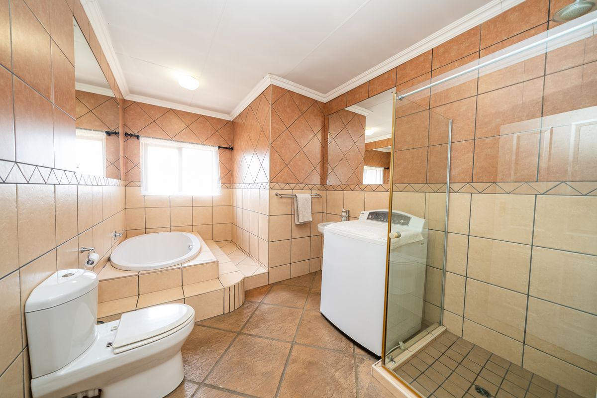 Spacious bathroom featuring a built-in corner bathtub, glass-enclosed shower, toilet, and integrated laundry area with tiled finishes throughout.