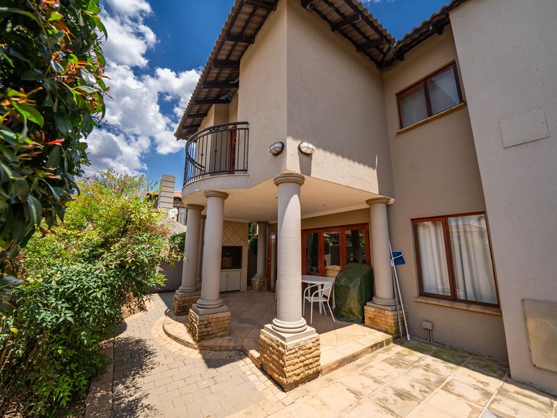 Covered patio area featuring classic columns, built-in braai, and an upper-level balcony, providing a functional outdoor entertainment space.