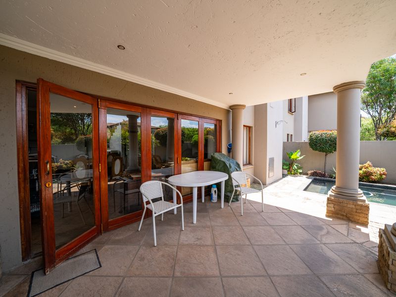 Covered patio area featuring tiled flooring, structural columns, and large wooden-framed glass doors leading into the home, adjacent to a small pool.