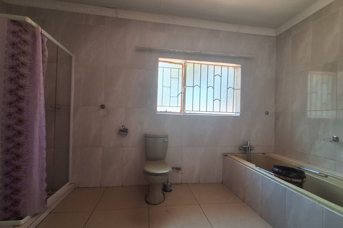 A dated bathroom featuring a built-in bathtub, separate shower enclosure, and tiled walls. The space requires cosmetic updates to modernize the fixtures and finishes.