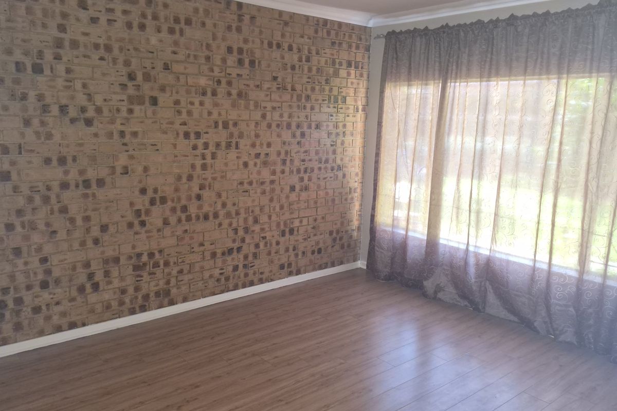 A living room featuring a prominent face-brick feature wall, wood-look laminate flooring, and large windows dressed with curtains.