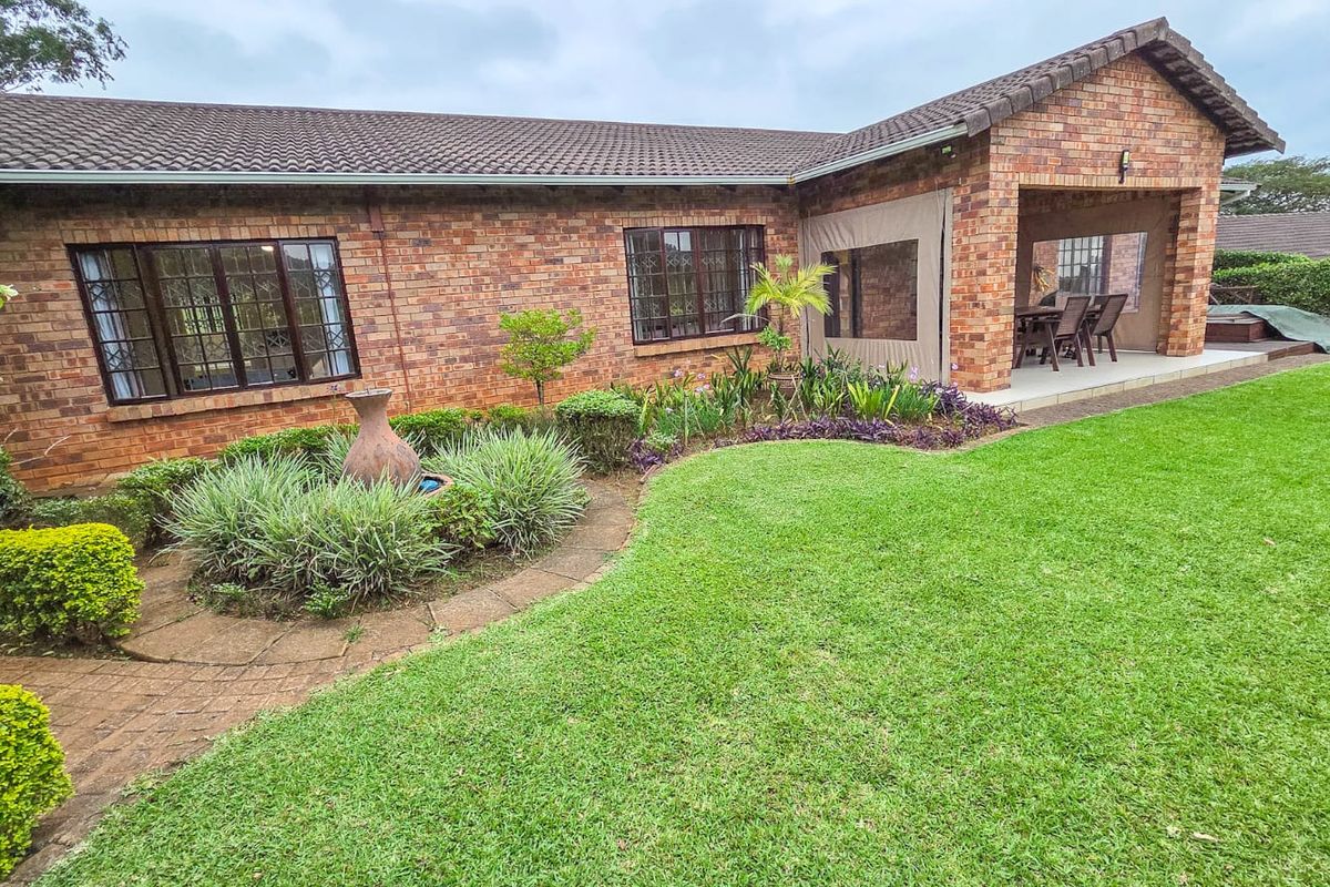 Rear view of a brick townhouse featuring a well-maintained garden, paved pathways, and a covered patio area.