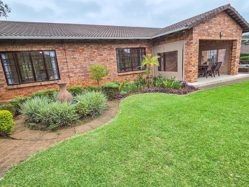 Rear view of a brick townhouse featuring a well-maintained garden, paved pathways, and a covered patio area.