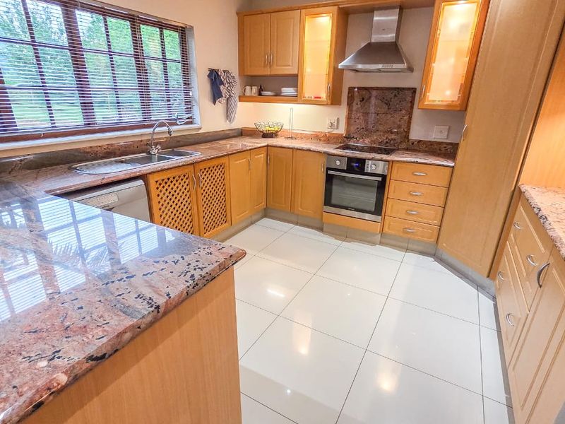 A functional kitchen featuring granite countertops, fitted wooden cabinetry, built-in oven with extractor fan, and polished tiled flooring.