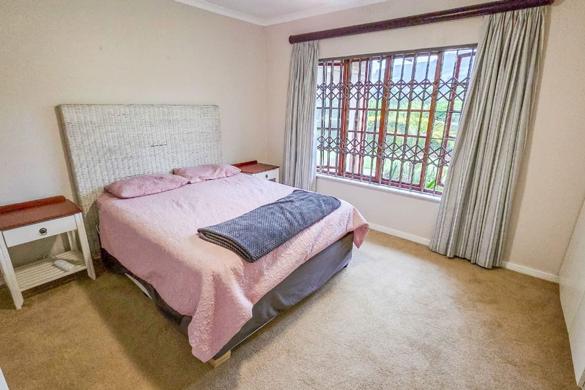 A carpeted bedroom featuring built-in cupboards and a window fitted with a security gate, offering a functional and comfortable living space.