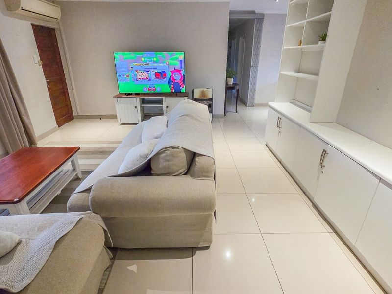 A spacious living room featuring large format floor tiles, extensive built-in cabinetry, and an integrated air conditioning unit.