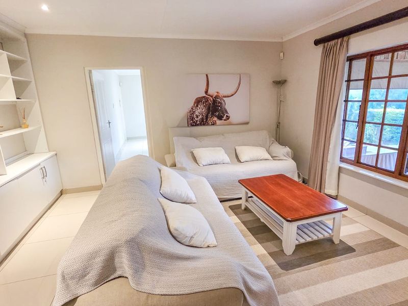 A comfortable living room featuring built-in cabinetry, tiled flooring, and large wooden-framed windows that provide natural light and a view of the patio.