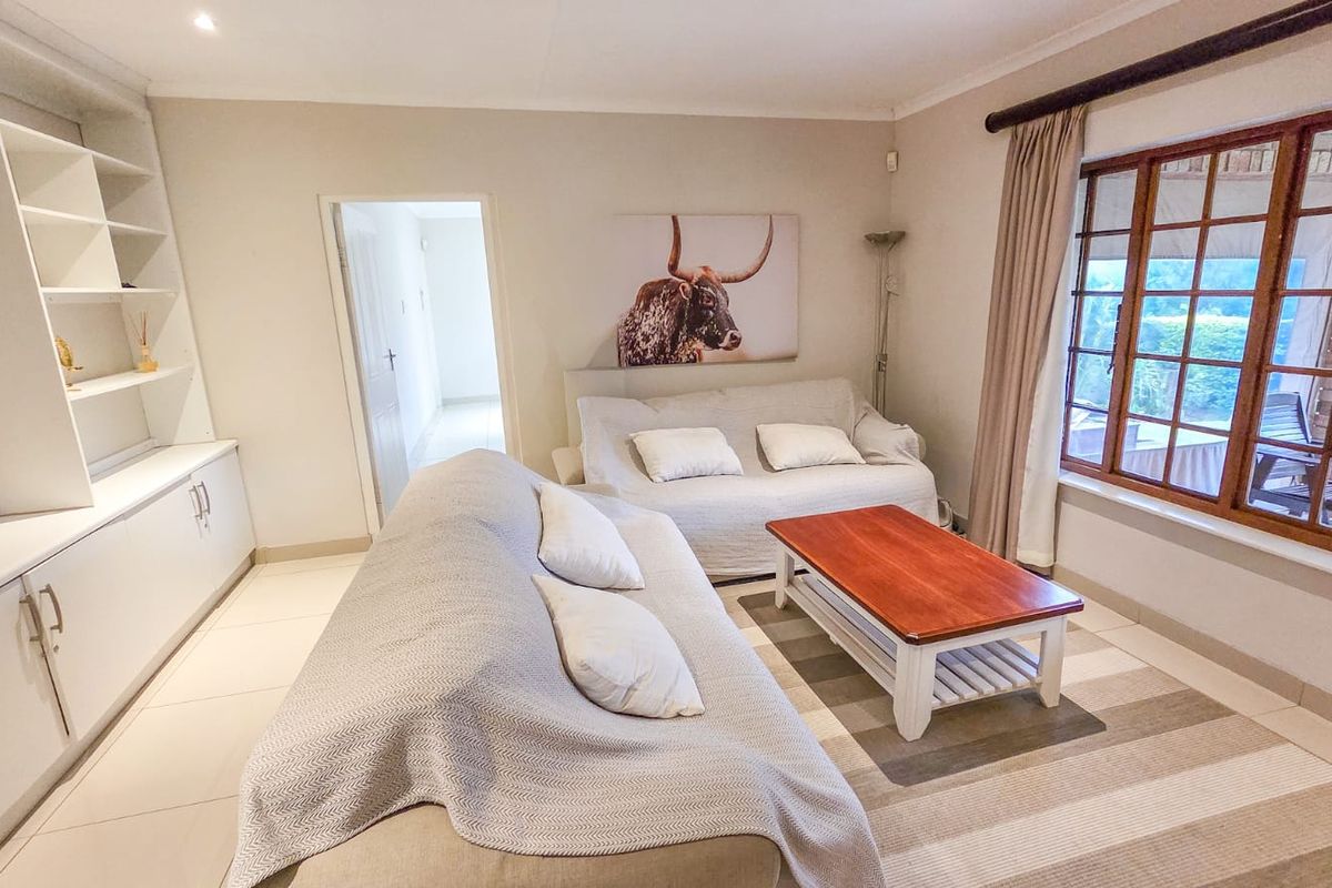 A comfortable living room featuring built-in cabinetry, tiled flooring, and large wooden-framed windows that provide natural light and a view of the patio.