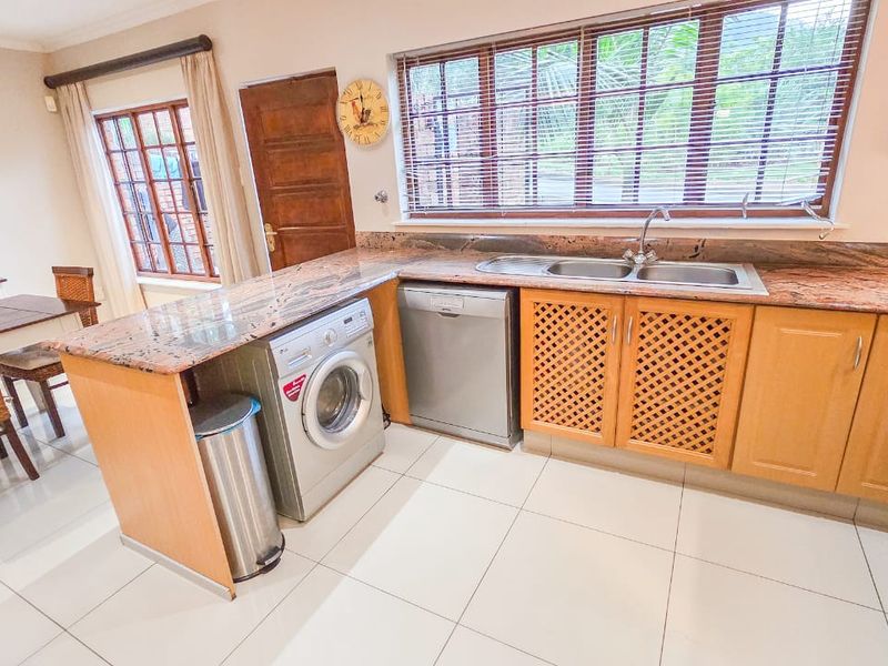 A functional kitchen featuring granite countertops, wooden cabinetry with lattice detailing, double basin sink, and tiled flooring, offering a practical workspace.