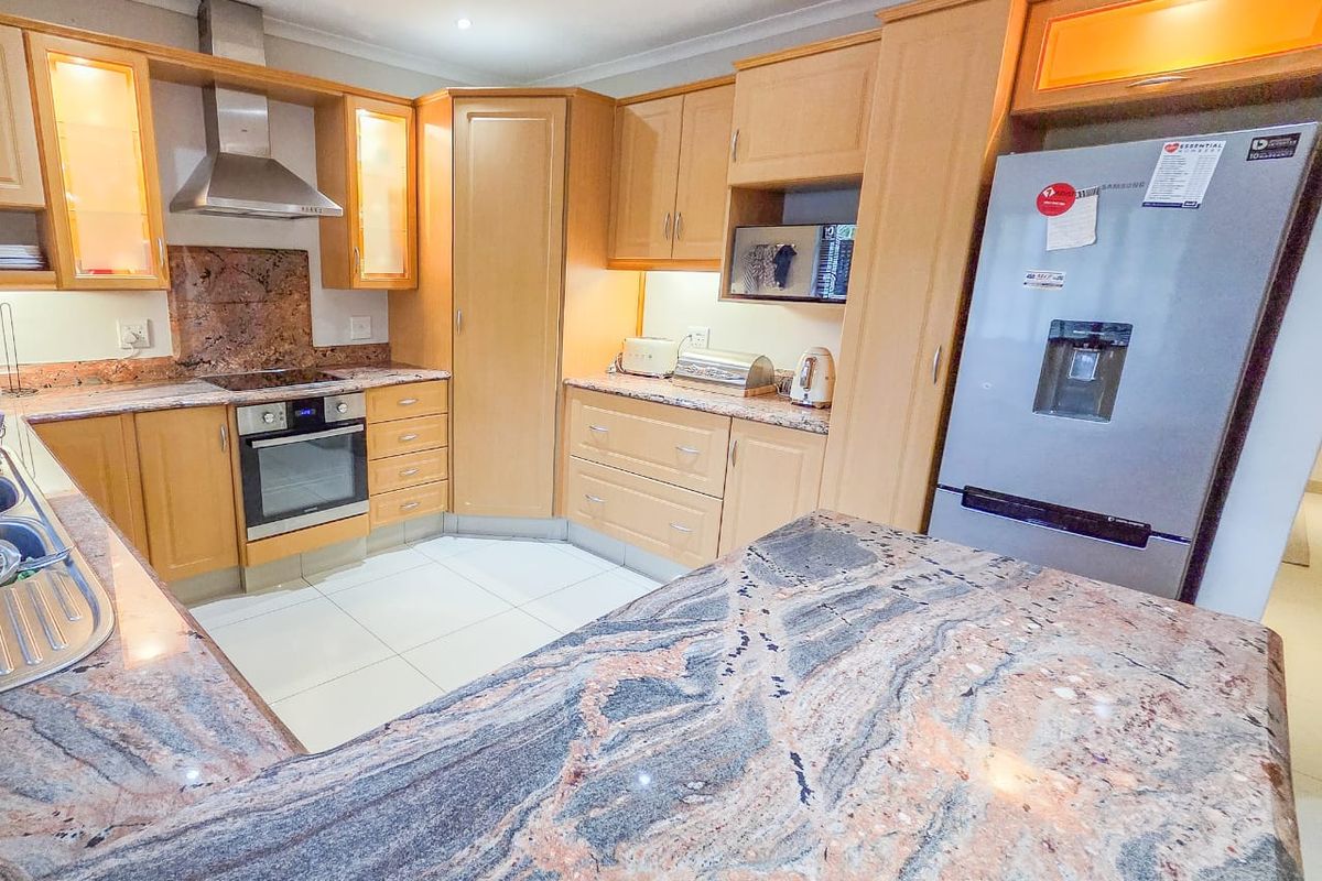 A well-maintained kitchen featuring light wood cabinetry, granite countertops, a built-in oven, and a stainless steel extractor fan.