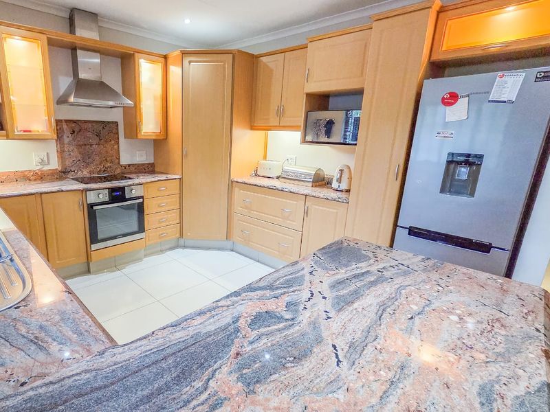 A well-maintained kitchen featuring light wood cabinetry, granite countertops, a built-in oven, and a stainless steel extractor fan.