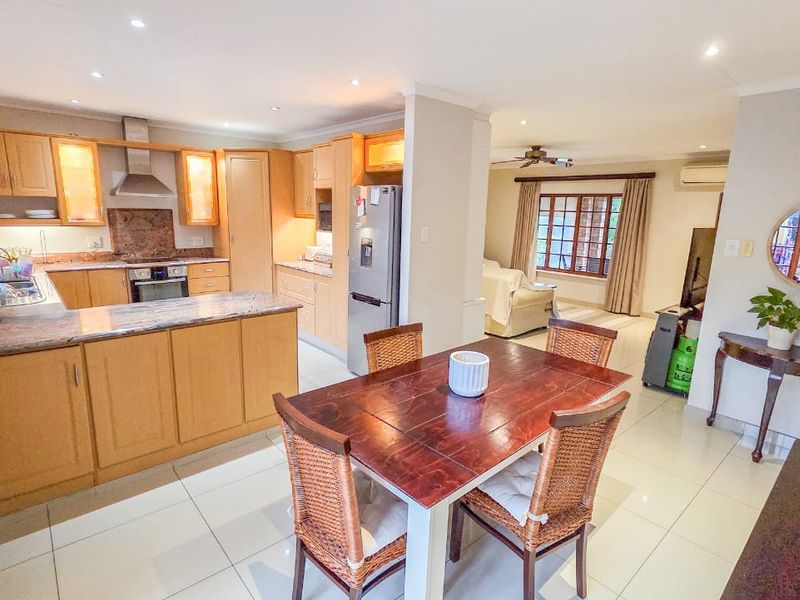 Open-plan kitchen and dining area featuring light wood cabinetry, granite countertops, tiled flooring, and recessed lighting, flowing into a connected living space.