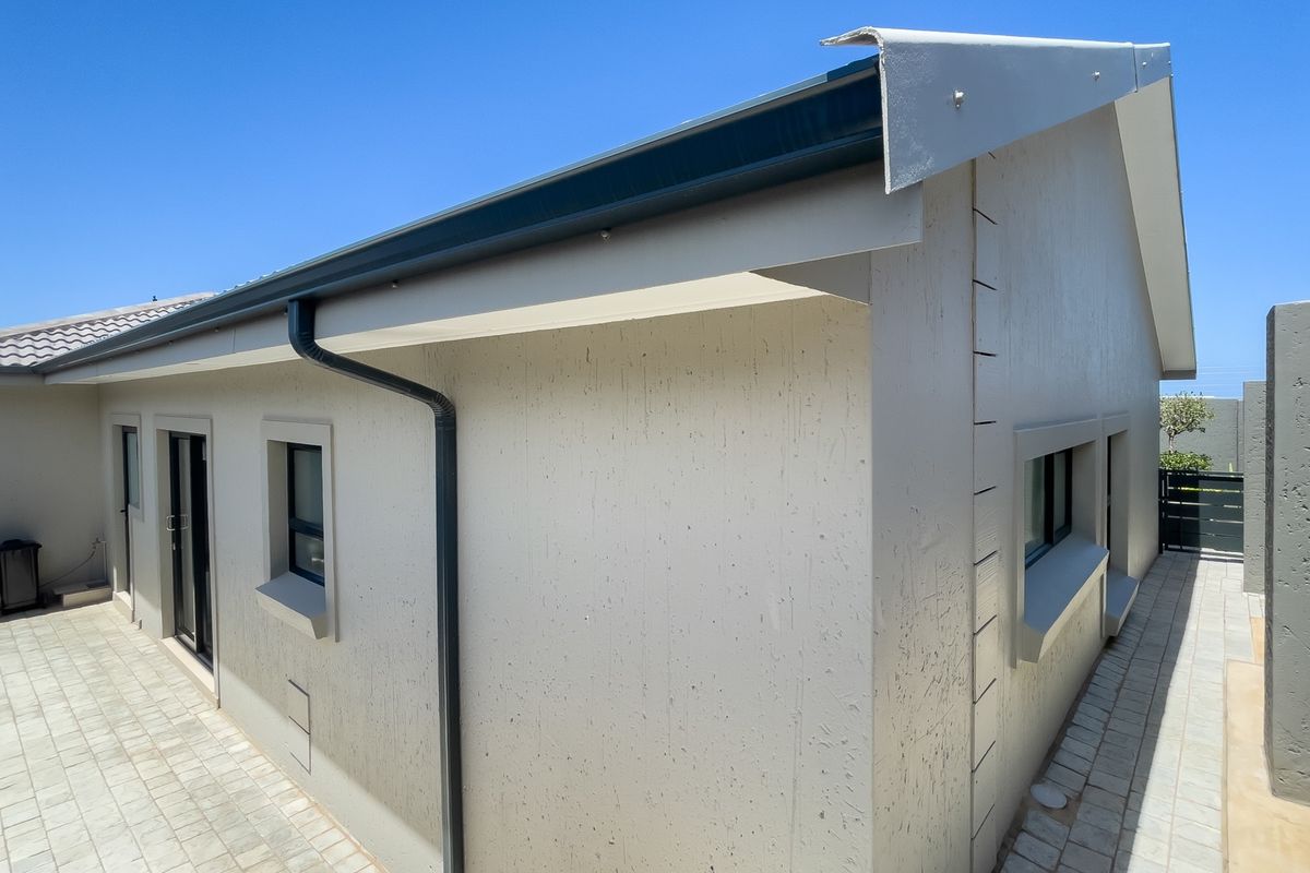 A view of the exterior rear elevation featuring paved walkways, modern textured wall finishes, and integrated guttering systems.