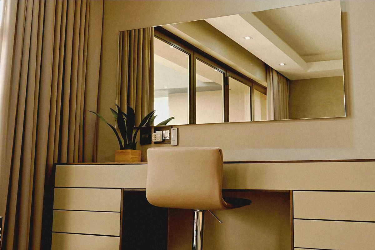 A well-appointed bedroom featuring a built-in vanity unit, large wall mirror, and recessed ceiling lighting, with access to a sliding glass door.
