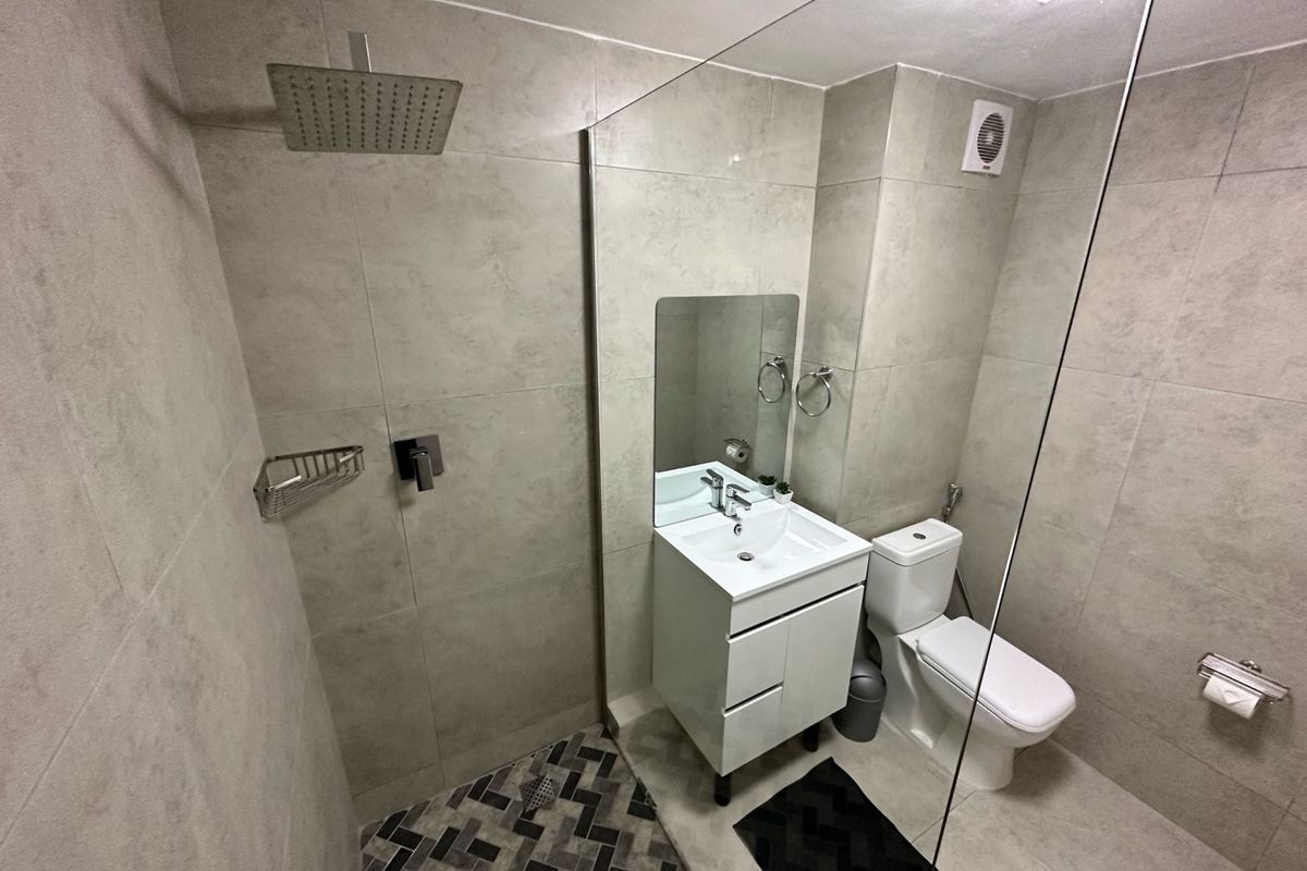 Modern bathroom featuring a walk-in shower with a rainfall showerhead, a vanity basin, and a toilet, finished with neutral wall and floor tiles.