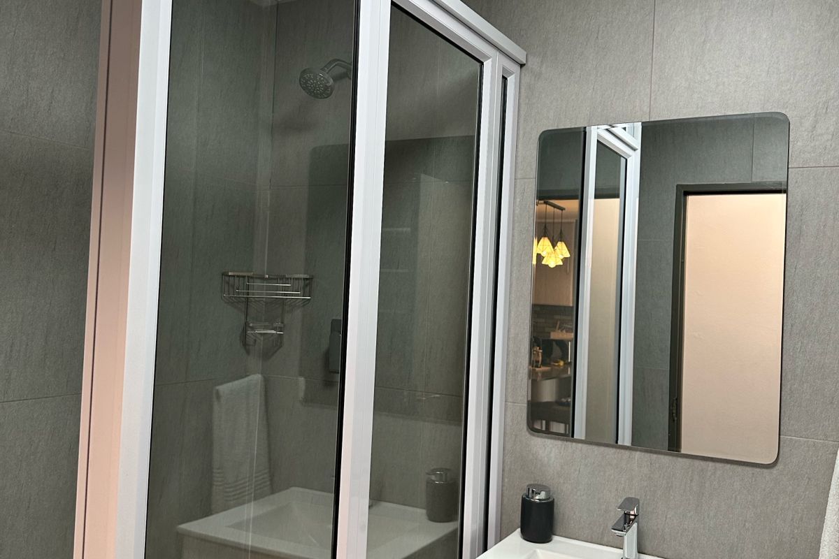 Modern bathroom featuring a glass-enclosed shower, a wall-mounted vanity with a basin, and neutral grey wall tiling.