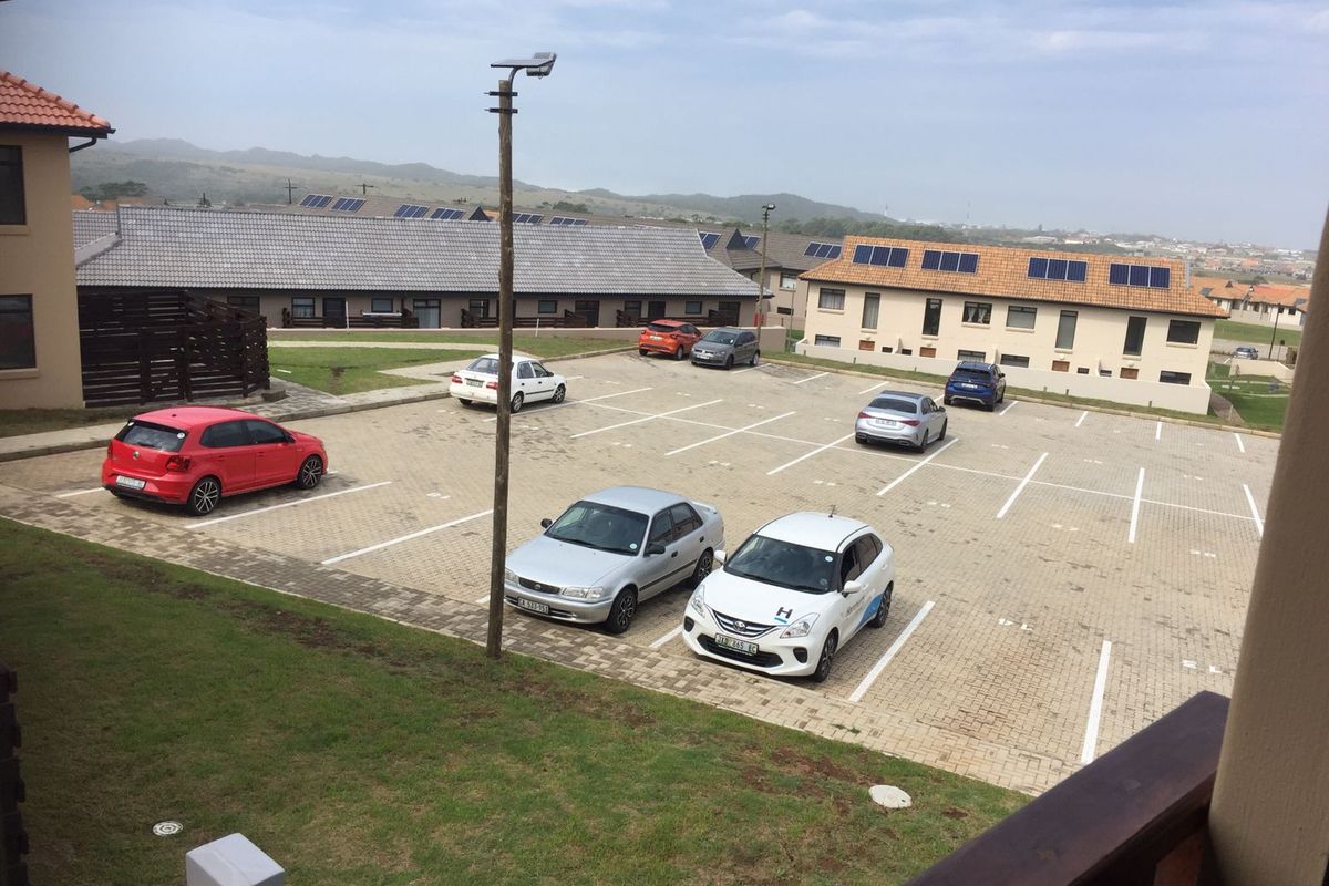 Elevated view of a paved communal parking area serving a townhouse complex with tiled roofs and solar installations.