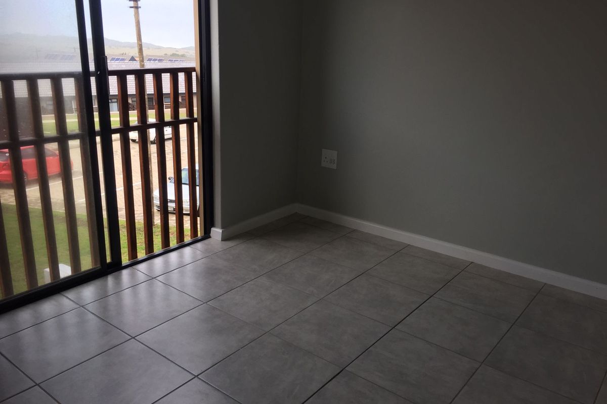 An empty bedroom featuring neutral grey tiled flooring, smooth walls, and a sliding glass door providing access to an outdoor area.