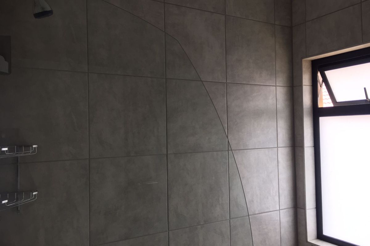 A modern bathroom shower area featuring neutral grey wall tiles, a fixed shower head, and a window for natural light.