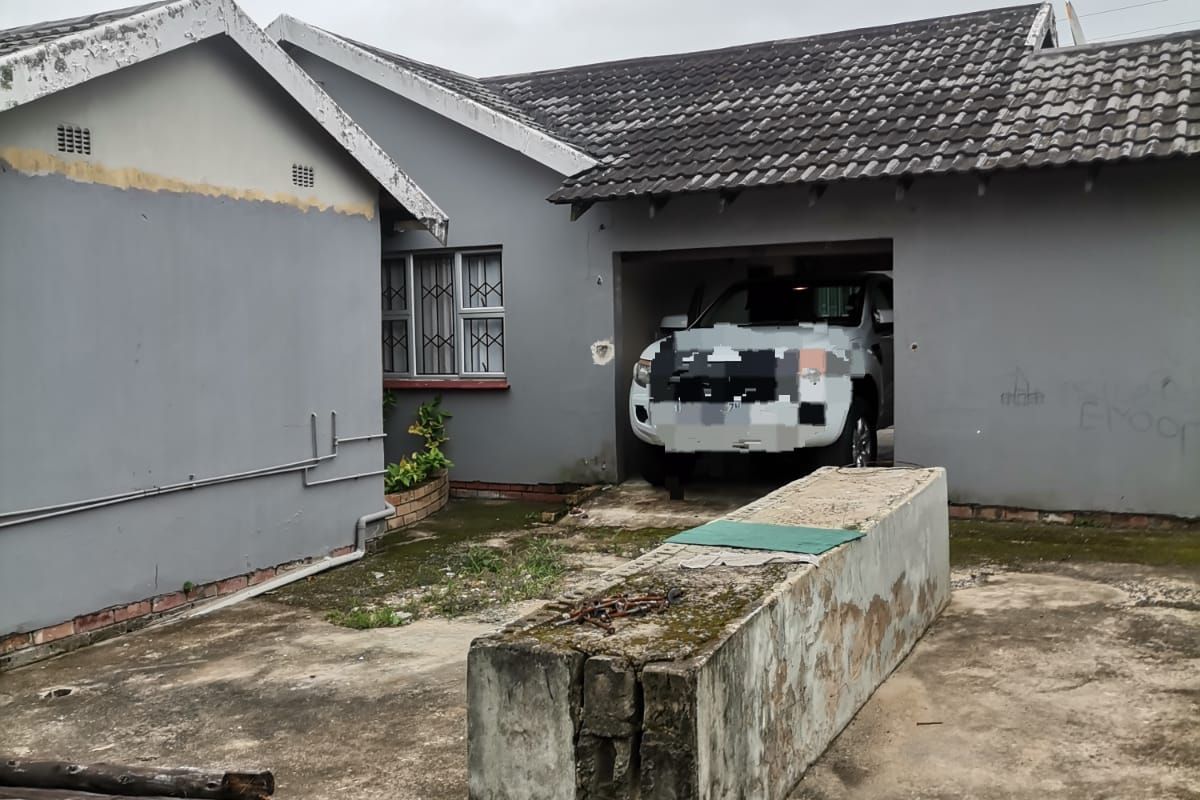 Exterior view of a residential property featuring a garage, concrete driveway, and weathered exterior walls requiring maintenance and cosmetic repairs.