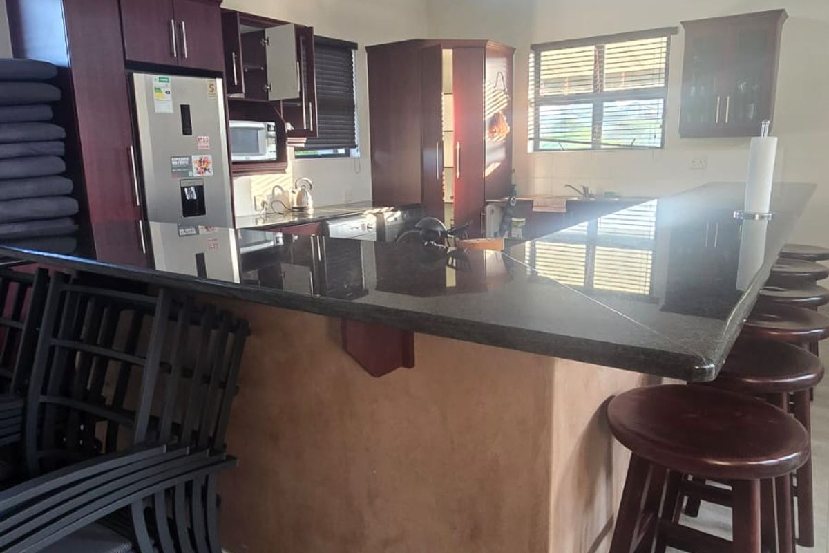 Spacious kitchen featuring a large granite-topped breakfast bar, dark wood cabinetry, vaulted ceilings with exposed beams, and tiled flooring.